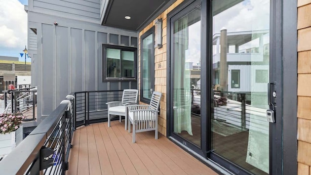 A balcony with a wooden floor, two white chairs, and a glass door. - Inspiration at The Cove Riverwalk Villas (Wilmington)