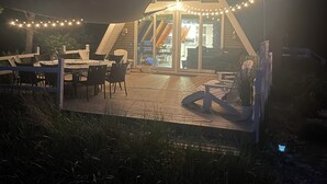 Uma casa moderna com telhado triangular, um deck com móveis de exterior e luzes de fada.