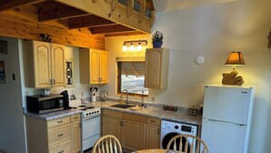 A compact kitchen with wooden cabinets, a stove, microwave, sink, and a refrigerator.