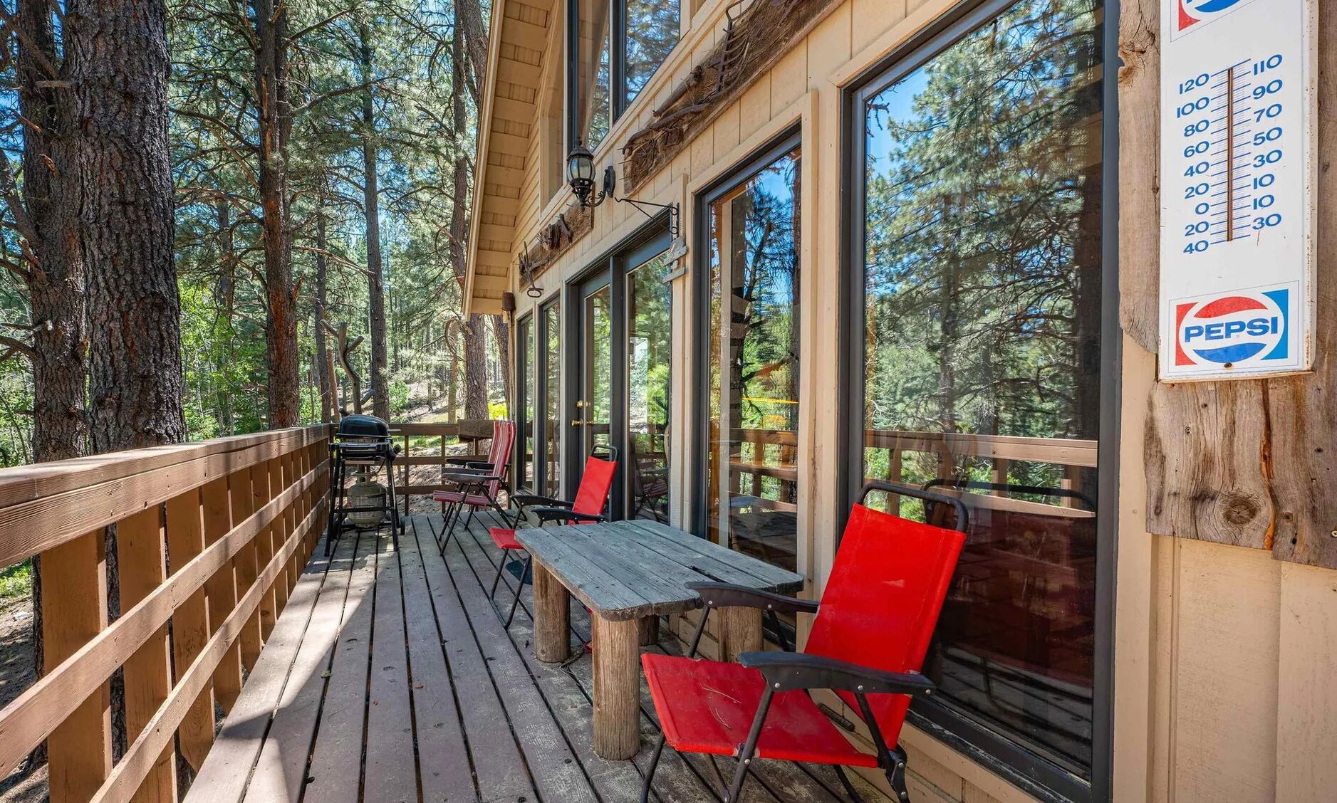 Una terraza exterior con bancos y sillas de madera, rodeada de árboles altos.