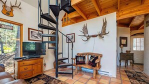 A rustic interior with a spiral staircase, wooden walls, antler decorations, a television, and a patterned rug.