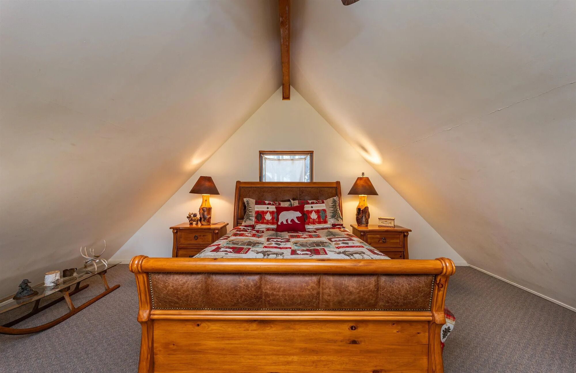 A bedroom with a sloped ceiling, a wooden bed with a quilt, two bedside lamps, and a small table with a lamp.