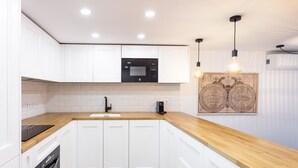 Une cuisine moderne avec des meubles blancs, un plan de travail en bois, un micro-ondes noir et une machine à café.