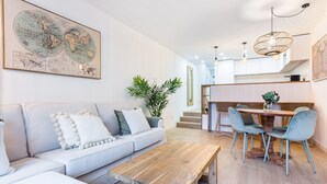 Un salon moderne avec un canapé, une table basse et un coin repas avec des chaises. On peut voir une carte du monde accrochée au mur et une plante dans un coin.