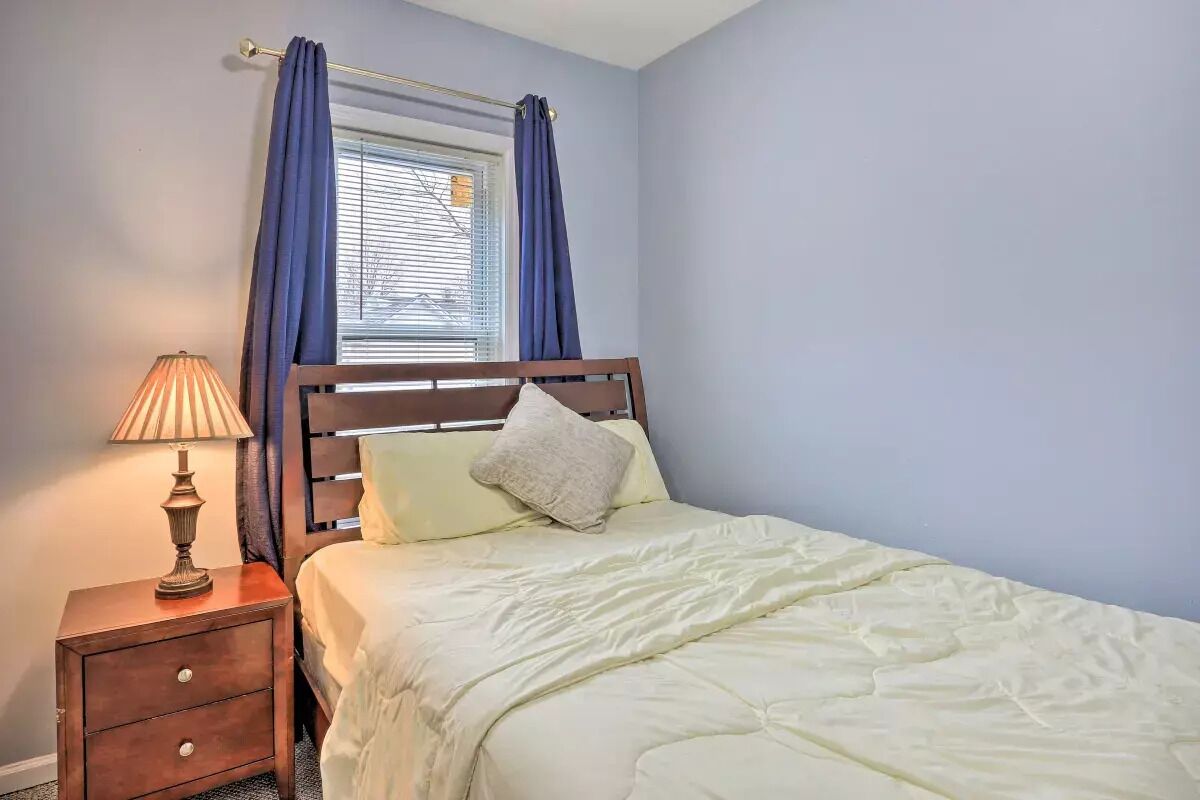 A bedroom with a bed, a nightstand with a lamp, and a window with curtains.