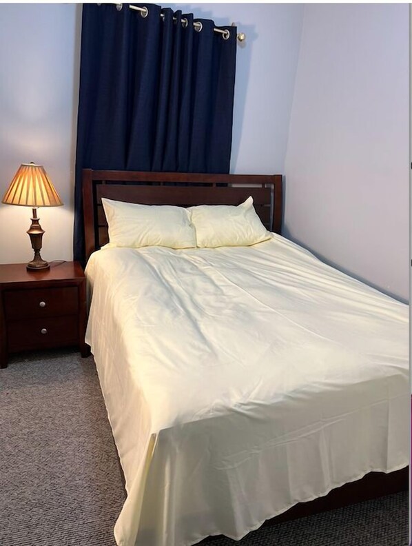 A neatly made bed with a wooden headboard, a bedside lamp, and a dark curtain.