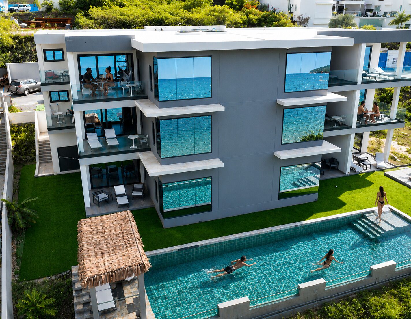 Un edificio moderno a più piani con piscina sul tetto, ampie finestre e un prato curato.