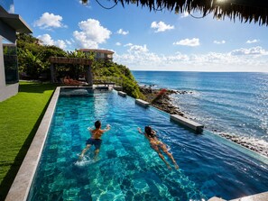 A swimming pool with clear blue water, a thatched roof structure, and a view of the ocean. - Condostmaarten appartment  right on the sea (Adults Only) (Sint Maarten)
