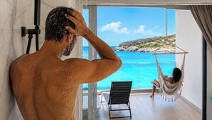 Un hombre en la ducha con vistas a una mujer en una hamaca junto a una piscina.