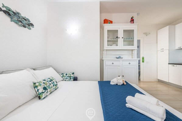 A hotel room with a bed, a blue quilt, white towels, a white cabinet with glass doors, and a small kitchen area.