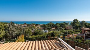 A coastal view from a rooftop terrace with terracotta tiles, overlooking a village with houses and trees, and the sea in the distance. - House Marisa - Seaview (Costa Rei)