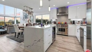 A modern kitchen with white cabinetry, a marble island, stainless steel appliances, and pendant lighting.