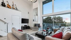 A modern living room with a fireplace, a flat-screen TV, and a large window overlooking a balcony.