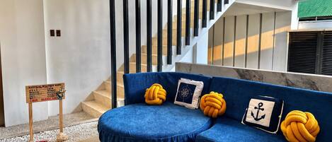 A modern interior with a blue sofa, nautical-themed cushions, a weather-themed sign, and a staircase.