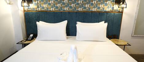Une chambre d’hôtel avec un grand lit, deux oreillers blancs, une tête de lit bleue, un mur à motifs et une table de chevet avec un téléphone.