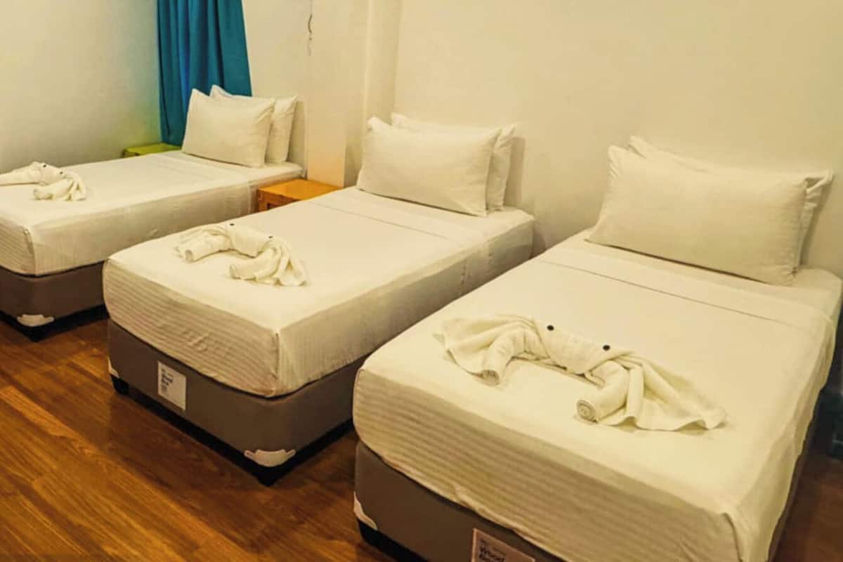 Three single beds with white linens and towels, wooden flooring, and a blue curtain in the background.