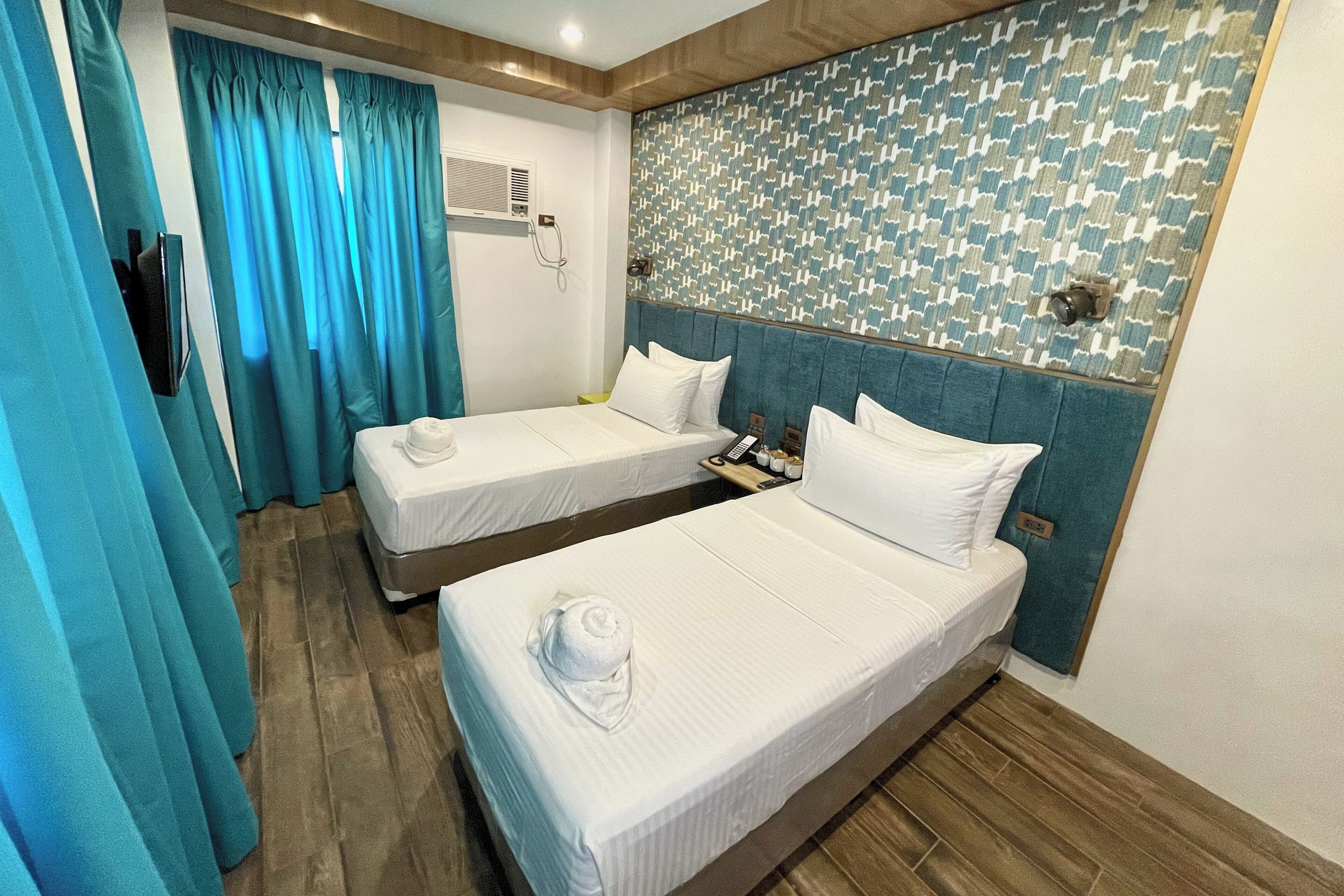 A hotel room with two beds, a patterned wall, and a wooden floor.