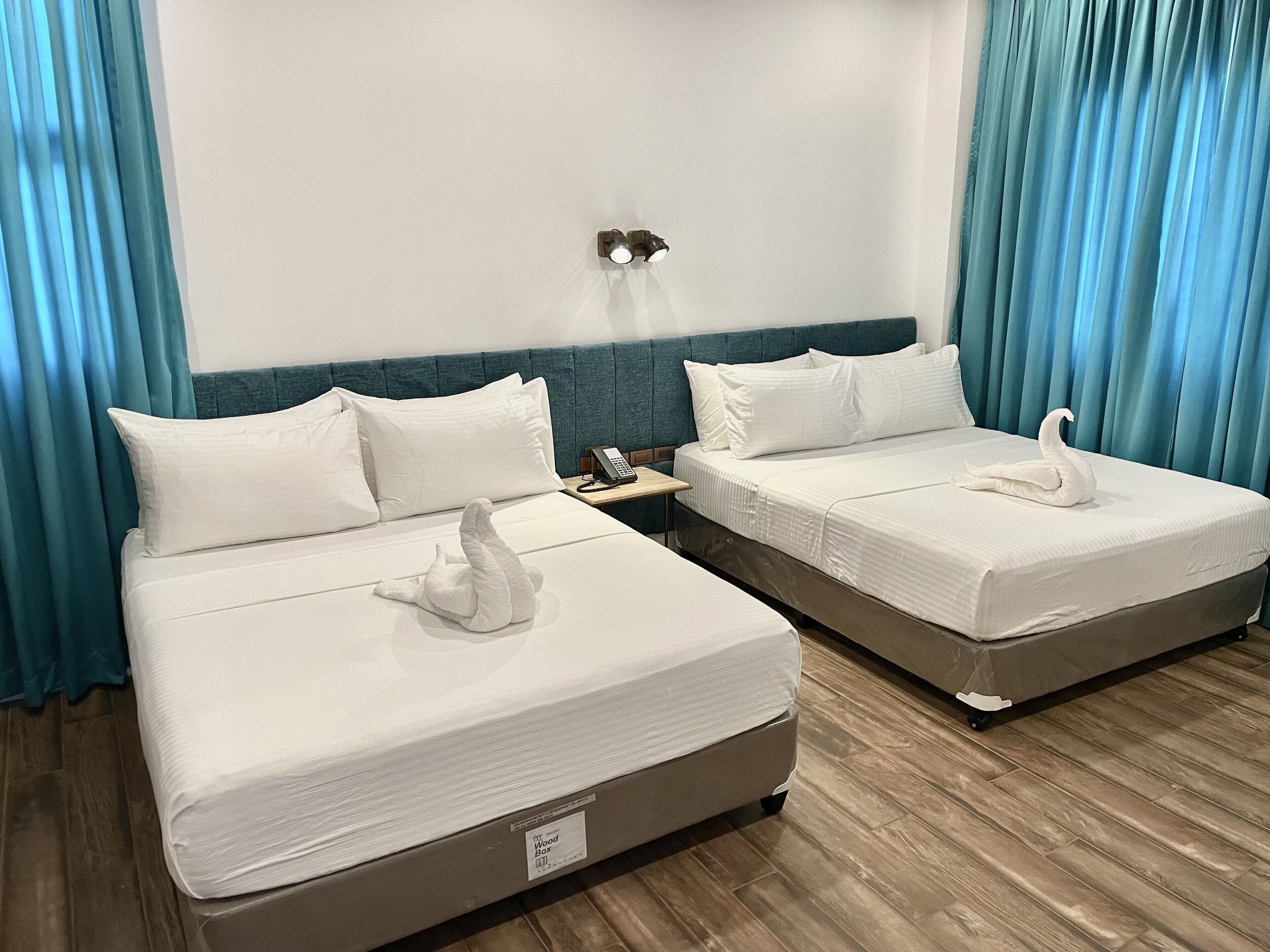 Two beds with white linens, a bedside table with a phone, and a wall-mounted light fixture.