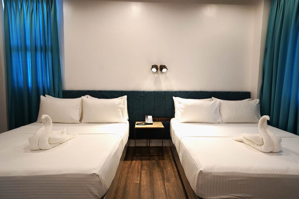 A hotel room with two beds, a small table with a telephone, and a wall-mounted light fixture.