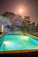 A nighttime pool area with a tiled floor, surrounded by trees and a fence.