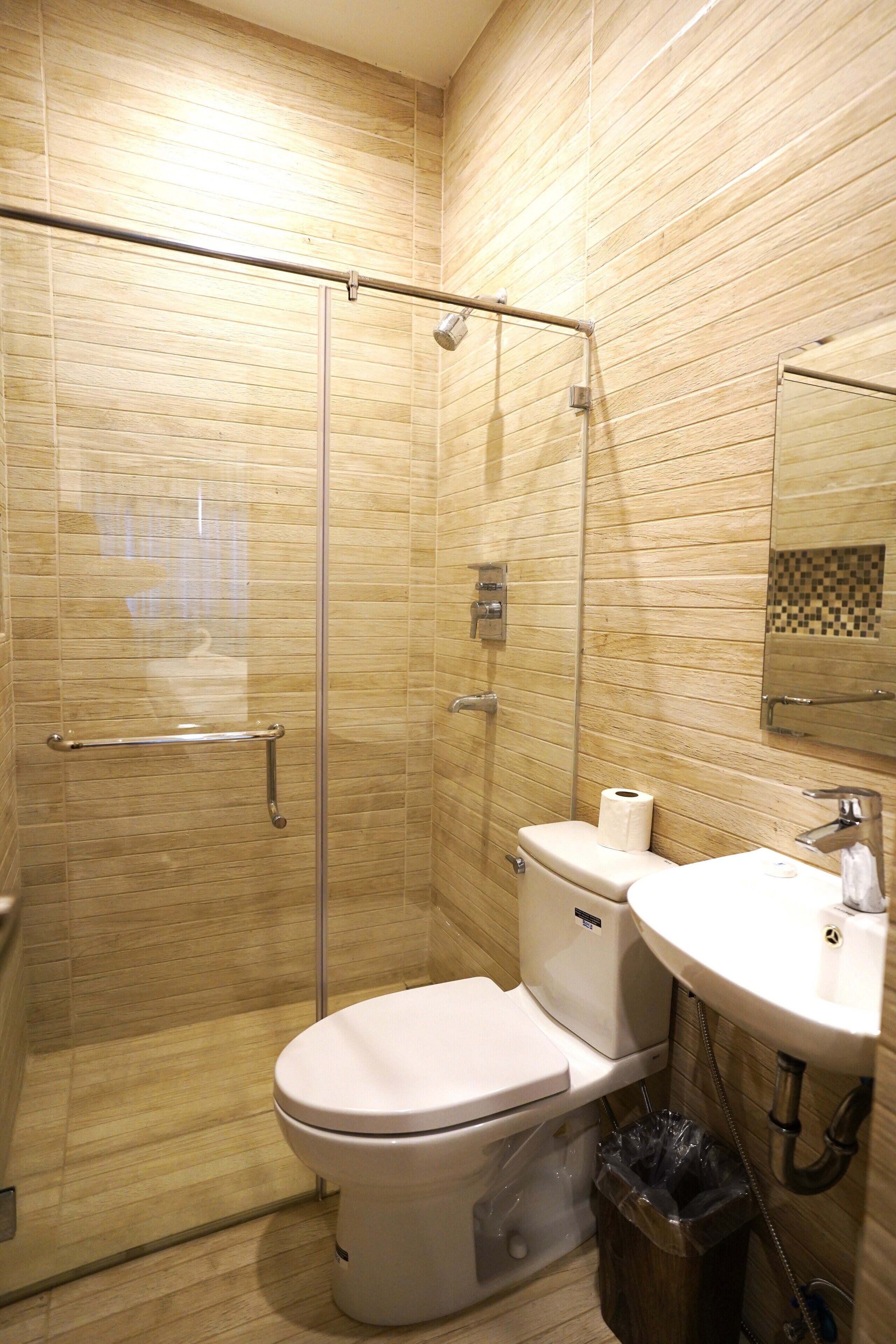 A bathroom with a glass-enclosed shower, a toilet, a sink, and a trash bin.