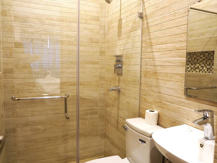 A bathroom with a glass-enclosed shower, a toilet, a sink, and a trash bin.