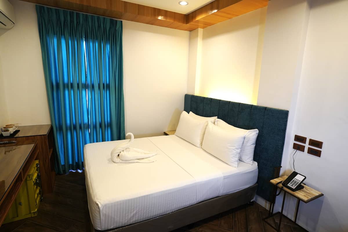 A hotel room with a bed, a desk, a telephone, and a window with curtains.
