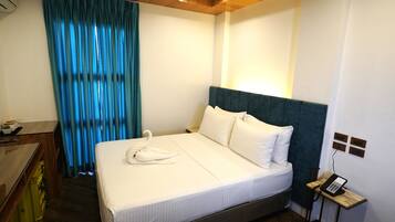 A hotel room with a bed, a desk, a telephone, and a window with curtains.
