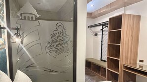 A hotel room with a bed, a bench, a wardrobe, and a glass door with a logo. - Lighthouse Point Hotel (Dumaguete)
