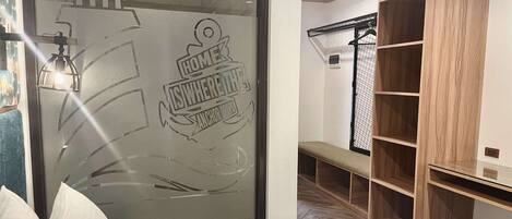 Habitación de hotel con cama, banca, armario y puerta de vidrio con un logotipo.