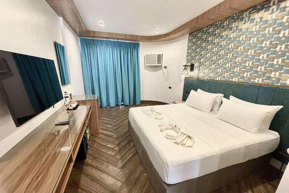 A hotel room with a large bed, a desk with a flat-screen TV, a blue curtain, and a patterned wall.