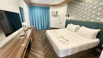 A hotel room with a large bed, a desk with a flat-screen TV, a blue curtain, and a patterned wall.