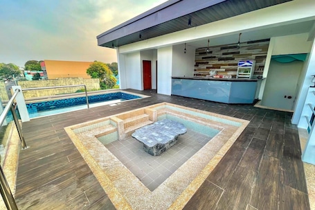 A modern outdoor pool area with a hot tub, a kitchen with a bar, and a view of the surrounding landscape.. Lighthouse Point Hotel
