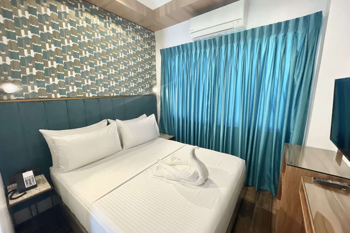 A neatly made bed with white linens, a patterned wall behind it, and a blue curtain to the right.