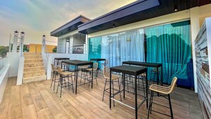 A modern outdoor patio with wooden flooring, metal tables, and wicker chairs. - Lighthouse Point Hotel (Dumaguete)
