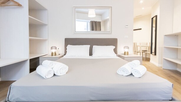 Een moderne hotelkamer met een groot bed, bedlampjes, een spiegel boven het bed en een kledingkast met ophanging.