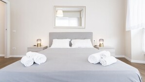 Un lit bien fait, avec du linge de lit blanc, une lampe de chevet et un miroir au mur.