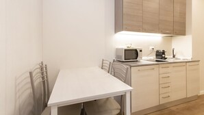 Une cuisine compacte avec une table blanche, deux chaises, un four à micro-ondes, une machine à café et des placards en bois.