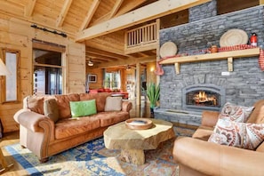 A cozy log cabin interior with a stone fireplace, leather sofas, and a wooden coffee table.