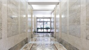 A corridor with marble walls and a tiled floor leading to a glass door with a view of outdoor plants. - S.Maria Valle Apartment 3 (Milano)