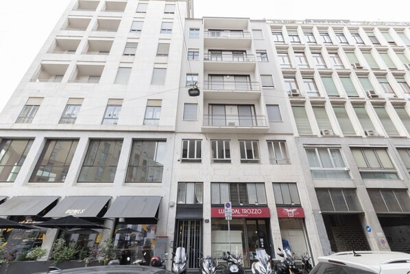 Un immeuble à plusieurs étages dont le rez-de-chaussée est occupé par des commerces, notamment un restaurant appelé « Lu D’al Trozzo », et dont la façade est ornée d’une enseigne indiquant « BOWLS ».
