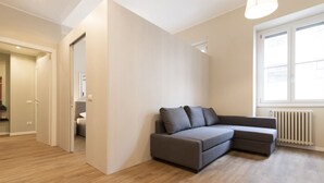 A modern living room with a grey sectional sofa, wooden flooring, a white radiator, and a window with blinds. - Missori Apartment 2  (Milano)