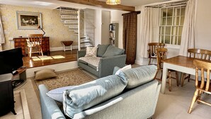 A living room with a sofa, a television, a dining table, and a staircase. - Orchard Cottage, Brayford (Brayford)