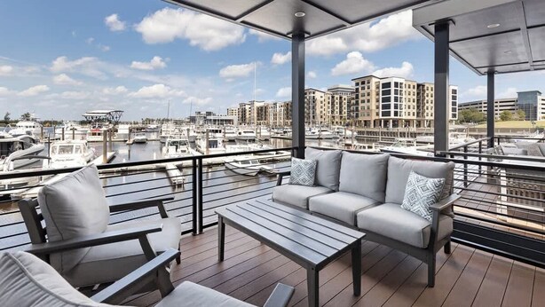 A balcony with a sofa and chairs, overlooking a marina with boats and buildings.
