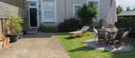 Propiedad residencial con patio empedrado, césped y un área de estar con mesa y sillas.