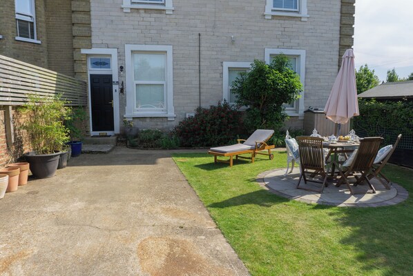 A residential property with a paved patio, a lawn, and a seating area with a table and chairs.