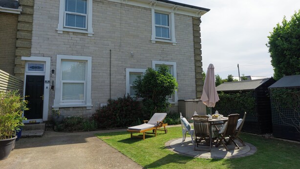 A two-story house with a patio area featuring a table and chairs, a small garden, and a black gate. - Lovely, spacious apartment - sleeps 5 (Ryde)