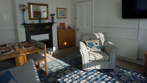 A living room with a fireplace, a television mounted on the wall, and a dining area with a table set for four. - Lovely, spacious apartment - sleeps 5 (Ryde)