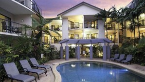 A hotel with a pool, lounge chairs, and a covered area with a pergola. - 5 mins walk to town and beach. Family sized top floor condo! (Port Douglas)