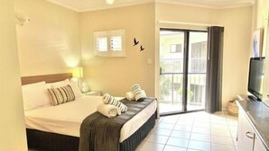 A hotel room with a bed, a TV, a balcony, and a ceiling fan. - 5 mins walk to town and beach. Family sized top floor condo! (Port Douglas)